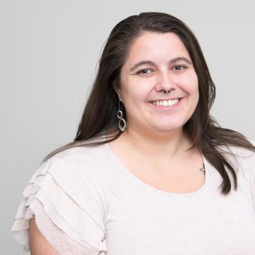 A person with long brown hair smiles for a portrait in front of a light grey background.