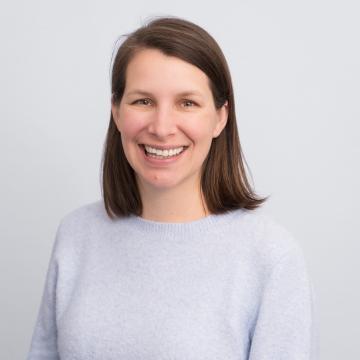 A person with brown hair smiles for a portrait in front of a light grey background.