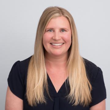 A person with long blonde hair smiles for a portrait in front of a light grey background.