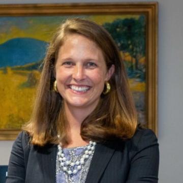 A woman smiles for a portrait in front of a painting.