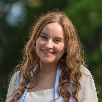 A person with curly hair smiles in front of a blurred green background.