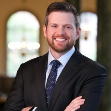 A person wearing a black suit smiles for a portrait. 