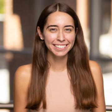 A person with long brown hair smiles in front of a blurred background.
