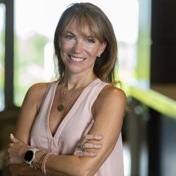 Person stands smiling with her arms crossed wearing a light shirt.