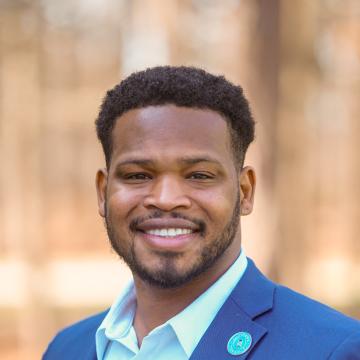 A man in a blue suit jacket smiles for a portrait. 