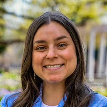Staff portrait of a smiling person with long brown hair wearing a blue jacket.