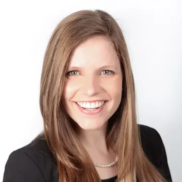 A person with long light brown hair smiles for a portrait in front of a white background.