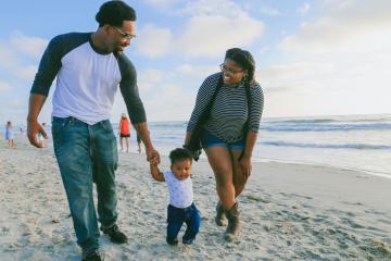 Two parents hold a child's hand while walking on a beach. 
