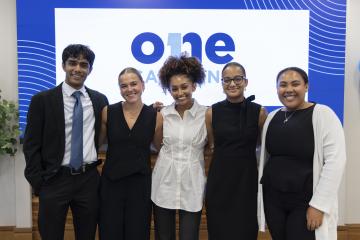 Five people stand and smile for a picture with a display that reads "One Carolina" in the background.