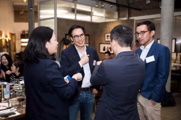 4 UNC alums in business casual attire talk to each other at an event