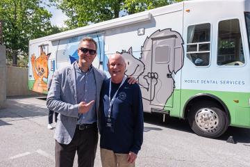 Two men stand in front of Mobile Dental Services bus