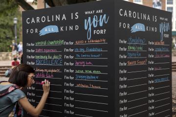 Student writes on a large chalkboard asking "What are you for?"