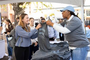 A student takes a tshirt from a faculty member at an on campus event