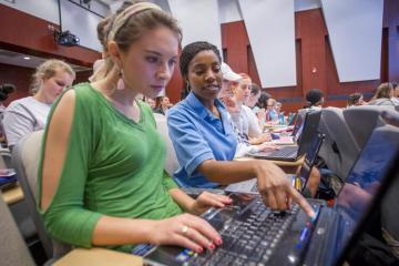 Students pointing to a laptop and having a discussion during a nursing class.