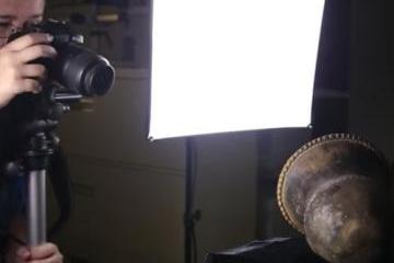 Person with camera takes photo of an ancient object sitting in front of a photo light. 
