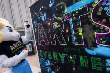 Rameses is painting an Arts Everywhere sign in the Pit. 