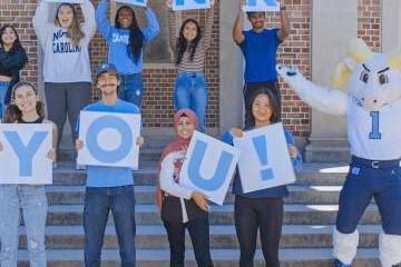 Students stand on the steps of a campus building holding up letters that spell Thank you!