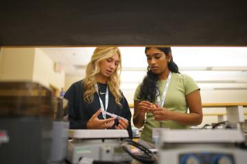 Two students work in a lab together. One holds a syringe.