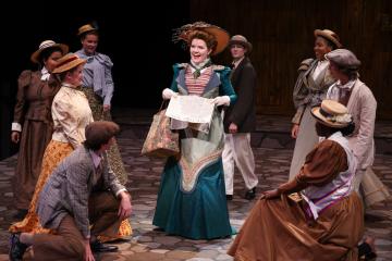 Cast of "Hello, Dolly!" performing on stage in Victorian-era costumes.