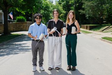 Three people stand in the street holding heat sensors and their covers.