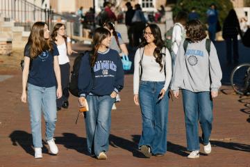 4 Carolina students walking along a sidewalk while talking to each other