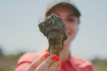 a woman holds up an oyster shell