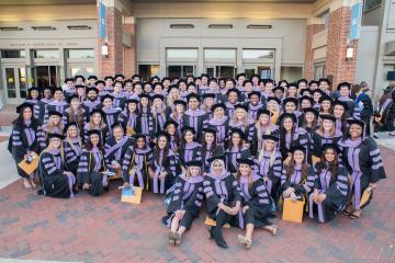 People in graduation regalia pose in front of the Adams School of Dentistry