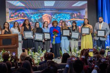 Students stand on stage holding certificates alongside Deloris P. Jordan.