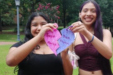Two students hold up two halves of a heart that spell out, "Best Duo."