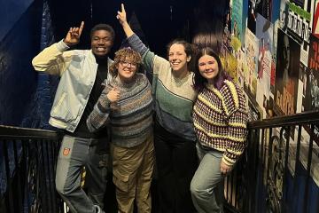 Carolina students and Aubrey Snowden, assistant teaching professor in the Department of Dramatic Art, pointing at a sign for 'The Making of a Broadway Show' exhibit while visiting New York City