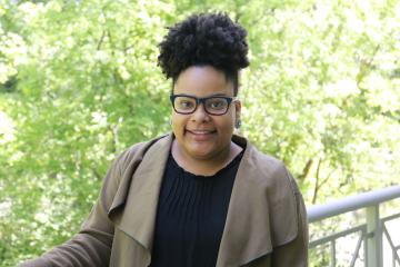 Elarnta Darden smiles and leans against a white railing with trees in the background.
