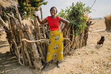 A woman stands in front of a fence in an arid landscape
