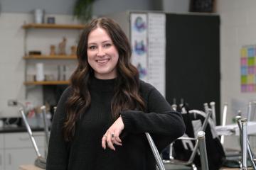 Molly Wells leans on an upside-down chair in a classroom