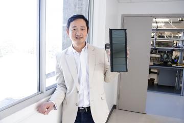 Jinsong Huang stands in a lab next to a window holding a solar panel