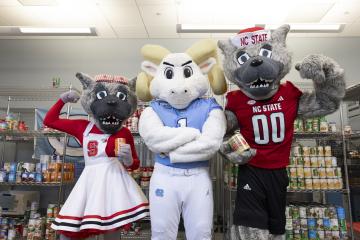 Carolina and NC State mascots pose looking forward while standing in a kitchen/pantry.