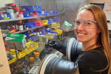 Charlotte Montgomery smiles for the camera while working in a fume hood and wearing protective glasses.