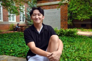 First-year Radian Hong poses for a sitting portrait outside, with Thomas Wolfe monument in backdrop.