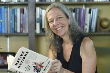 Portrait of Kathleen Duval reading book against library backdrop.