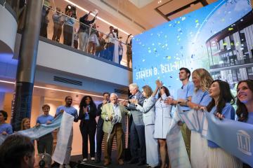 A group of stakeholders clap joyfully in front of a Bell Hall sign at the opening of Bell Hall.