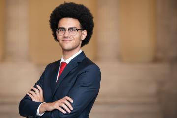 Adam Sherif stands with hands crossed wearing a suit