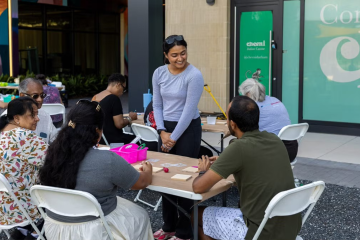 Person stands at a group of table with two others.