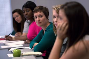 A Carolina student sits at a table in a classroom and looks at someone speaking
