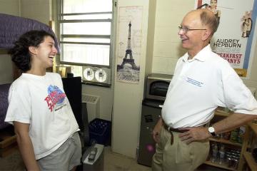 Two people smile and laugh together in a dorm room.