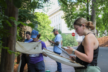 A group of researchers hold field equipment while standing on campus in front of trees.
