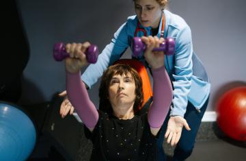 Eli Levene lifts arm weights while lying on a bench with the help of Gabby Brennan.