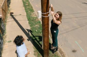 Two people set up a heat sensor and its cover on a telephone pole.
