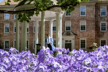 A Carolina graduate in commencement regalia stands at the Old Well.