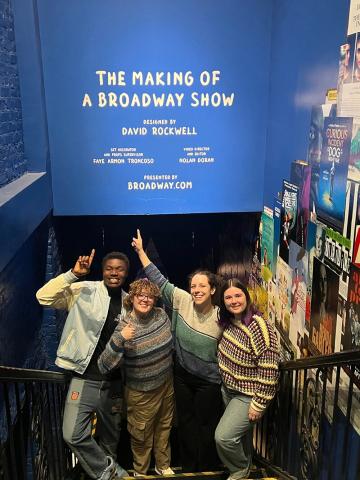 Carolina students and Aubrey Snowden, assistant teaching professor in the Department of Dramatic Art, pointing at a sign for 'The Making of a Broadway Show' exhibit while visiting New York City