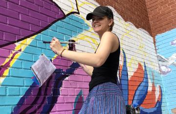 Chandler Simpson paints a mural on a brick wall.