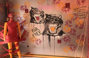 Closeup of a wall mural that depicts two tigers and sustainable fashion messaging with a mannequin in front of the wall wrapped up in red ribbons with its face covered.